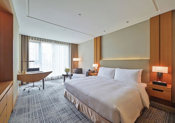 A hotel room with a large bed, a desk, a chair, and a small table with a lamp. - Millennium Hotel Taichung (Taichung)
