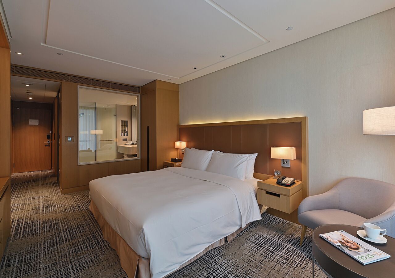 Ett hotellrum med en stor säng, sängbord, en stol och en tidning på bordet bredvid sängen.