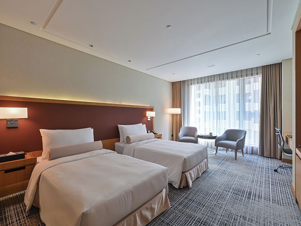 A hotel room with two beds, a desk, a chair, and a small table.