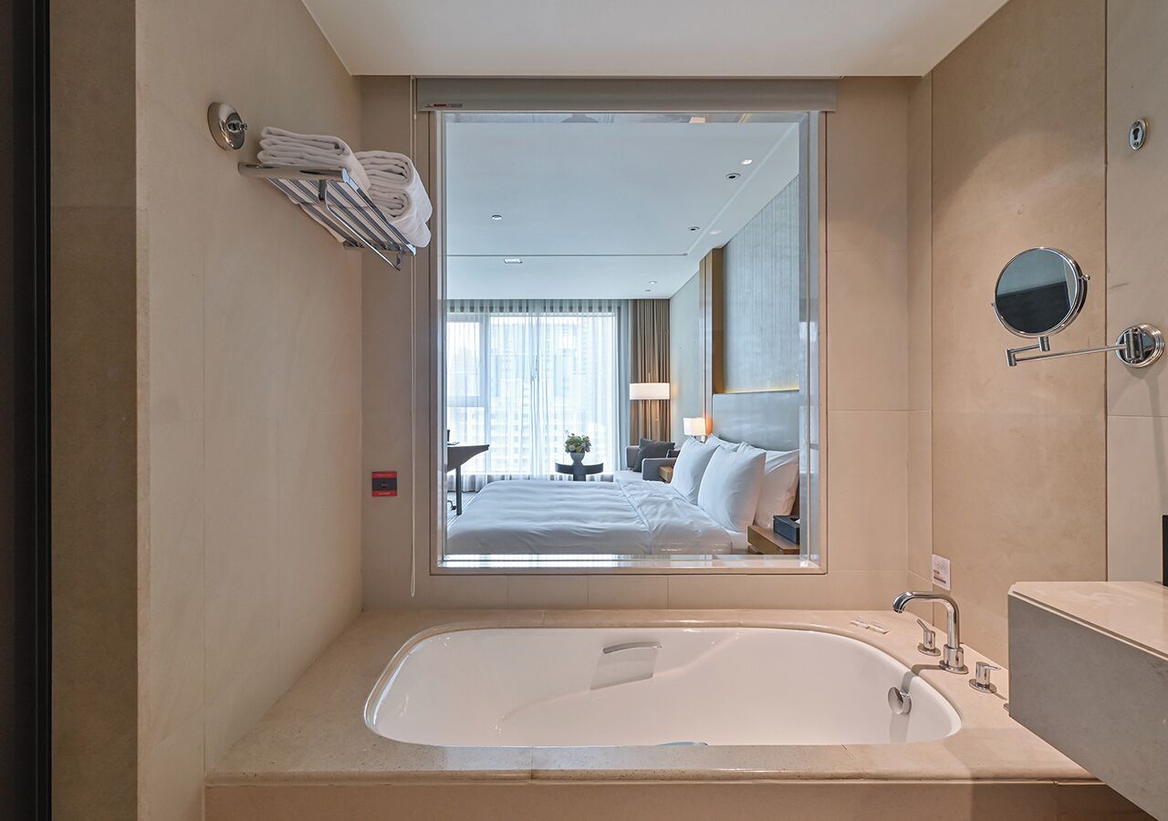 Un baño moderno con una bañera grande, un espejo y vistas de un dormitorio a través de una ventana.