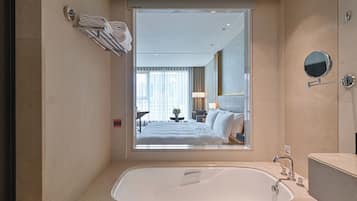 Un baño moderno con una bañera grande, un espejo y vistas de un dormitorio a través de una ventana.