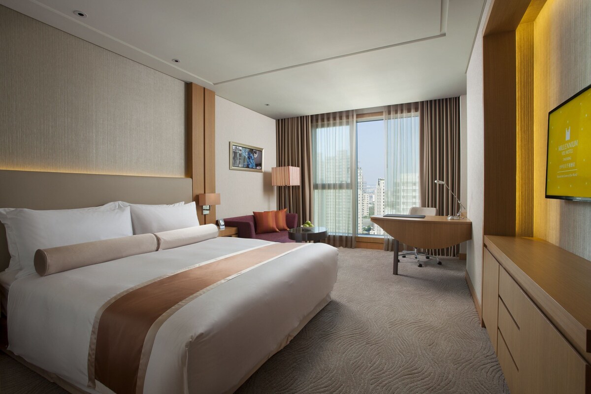 Habitación de hotel con una cama grande, un escritorio, una silla, un televisor y vistas a la ciudad.