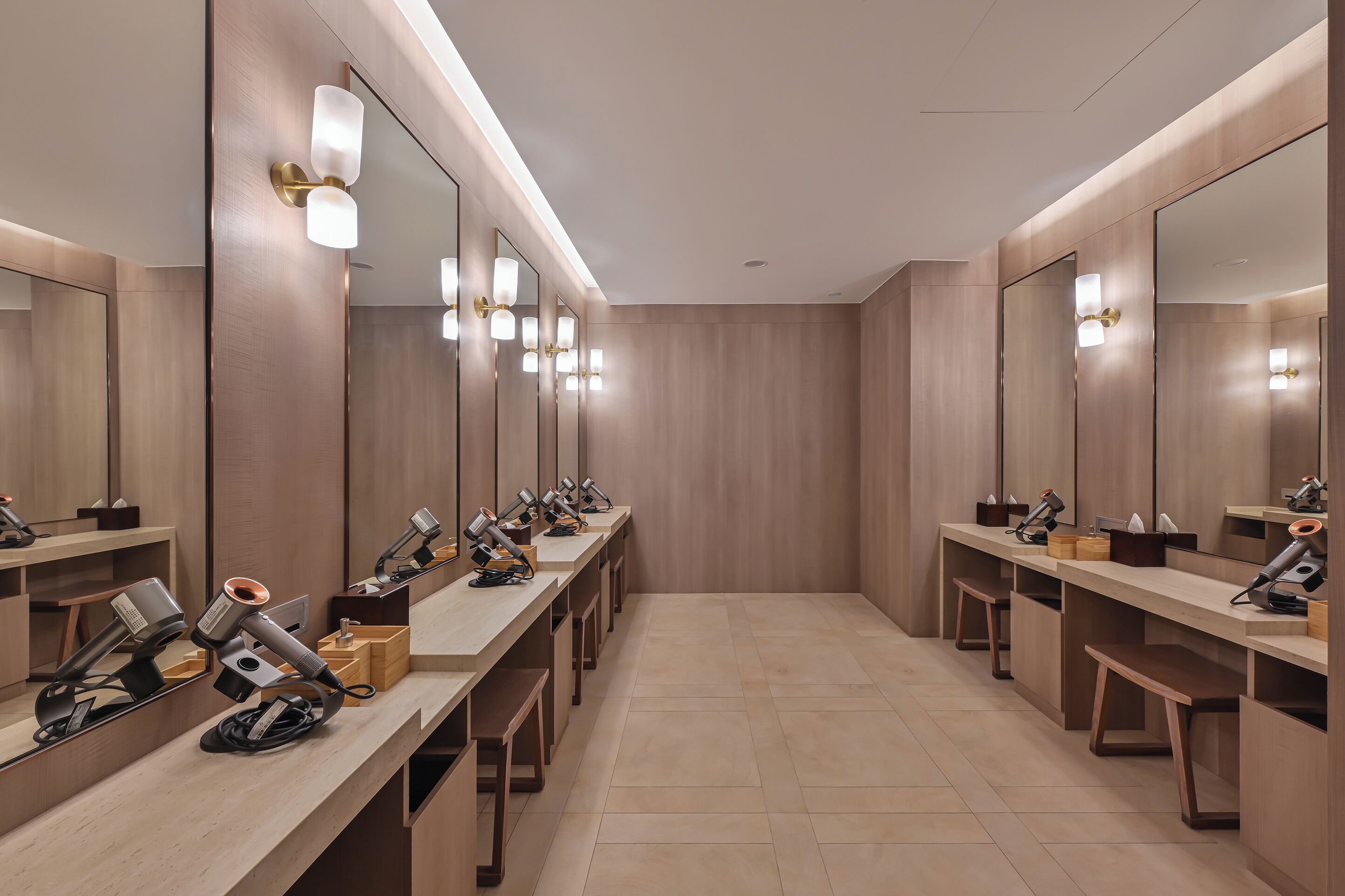 Un baño moderno con varios lavamanos, espejos y secadores de pelo.