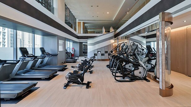 Un gimnasio moderno con cintas de correr, bicicletas estáticas y un nivel intermedio con vistas a la ciudad.
