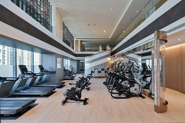Un gimnasio moderno con cintas de correr, bicicletas estáticas y un nivel intermedio con vistas a la ciudad.