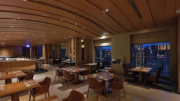A modern hotel lobby with a curved wooden ceiling, multiple seating areas, and a view of the cityscape through large windows.