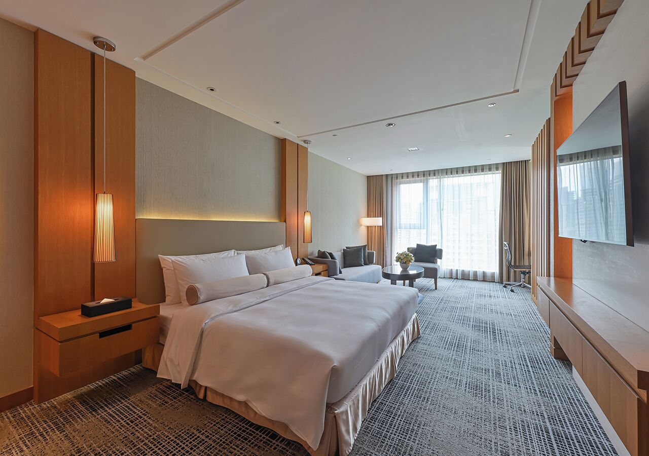 Una habitación de hotel con una cama grande, un escritorio, una silla, un televisor y una ventana con cortinas.