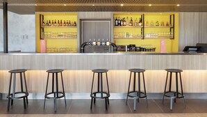 A bar area with a wooden ceiling, a counter with a drink tap, shelves with bottles and glasses, and four stools. - ibis Douai Dechy (Dechy)