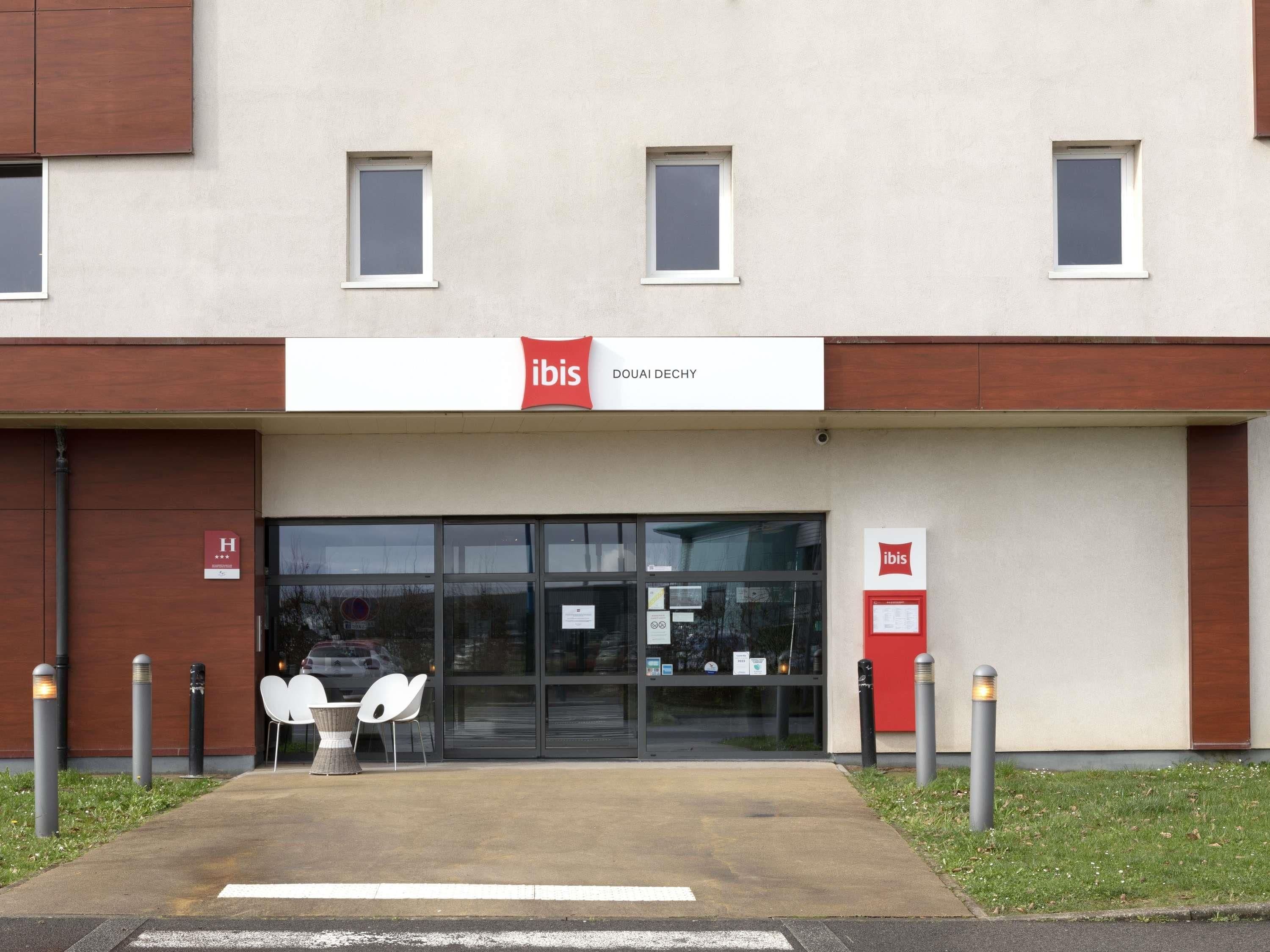 Un bâtiment moderne, avec une enseigne « ibis », une entrée en verre et des places assises à l’extérieur.