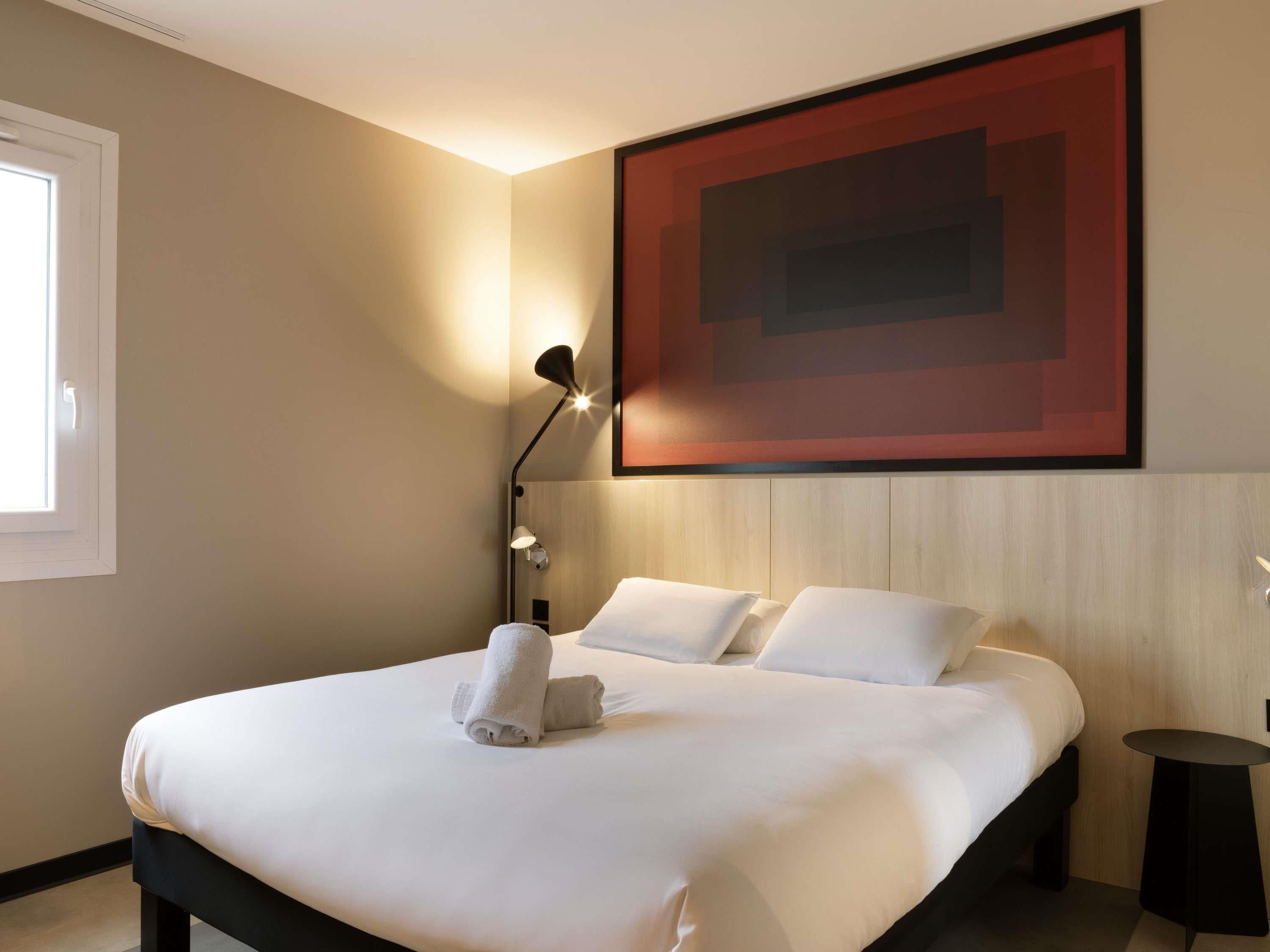 Ein Hotelzimmer mit einem großen Bett, einem Wandbild, einer Nachttischlampe und einem kleinen Tisch.