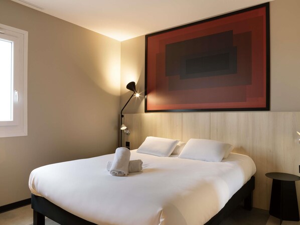A hotel room with a large bed, a wall-mounted artwork, a bedside lamp, and a small table.