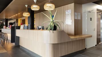 A modern reception desk with a wooden finish, a potted plant, and a sign indicating room rates.
