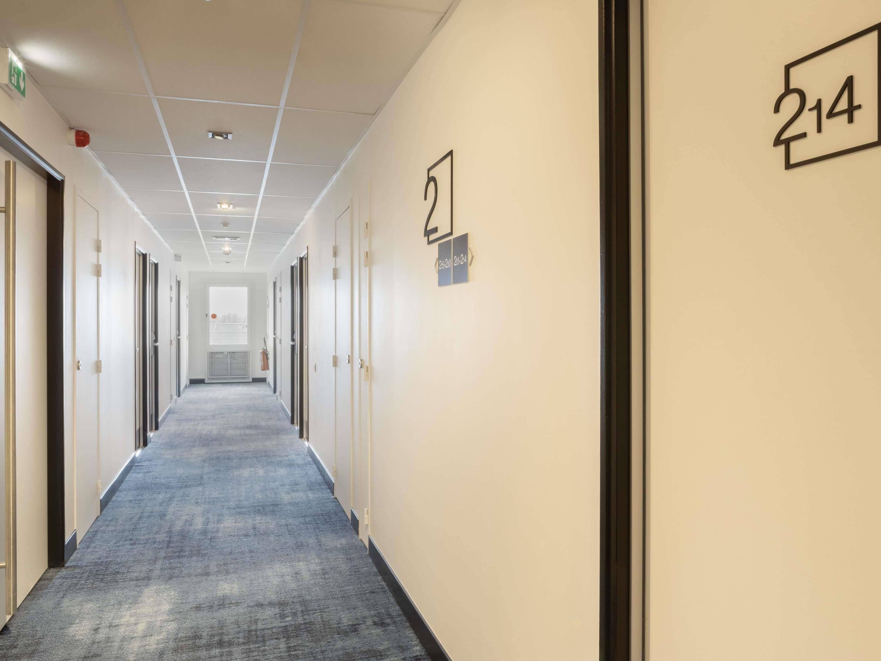 A hallway with doors numbered 214 and 215, carpeted floor, and a ceiling with recessed lighting.