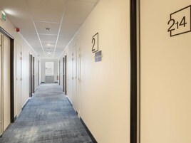Un pasillo con puertas numeradas 214 y 215, piso cubierto de alfombra e iluminación empotrada en el techo.