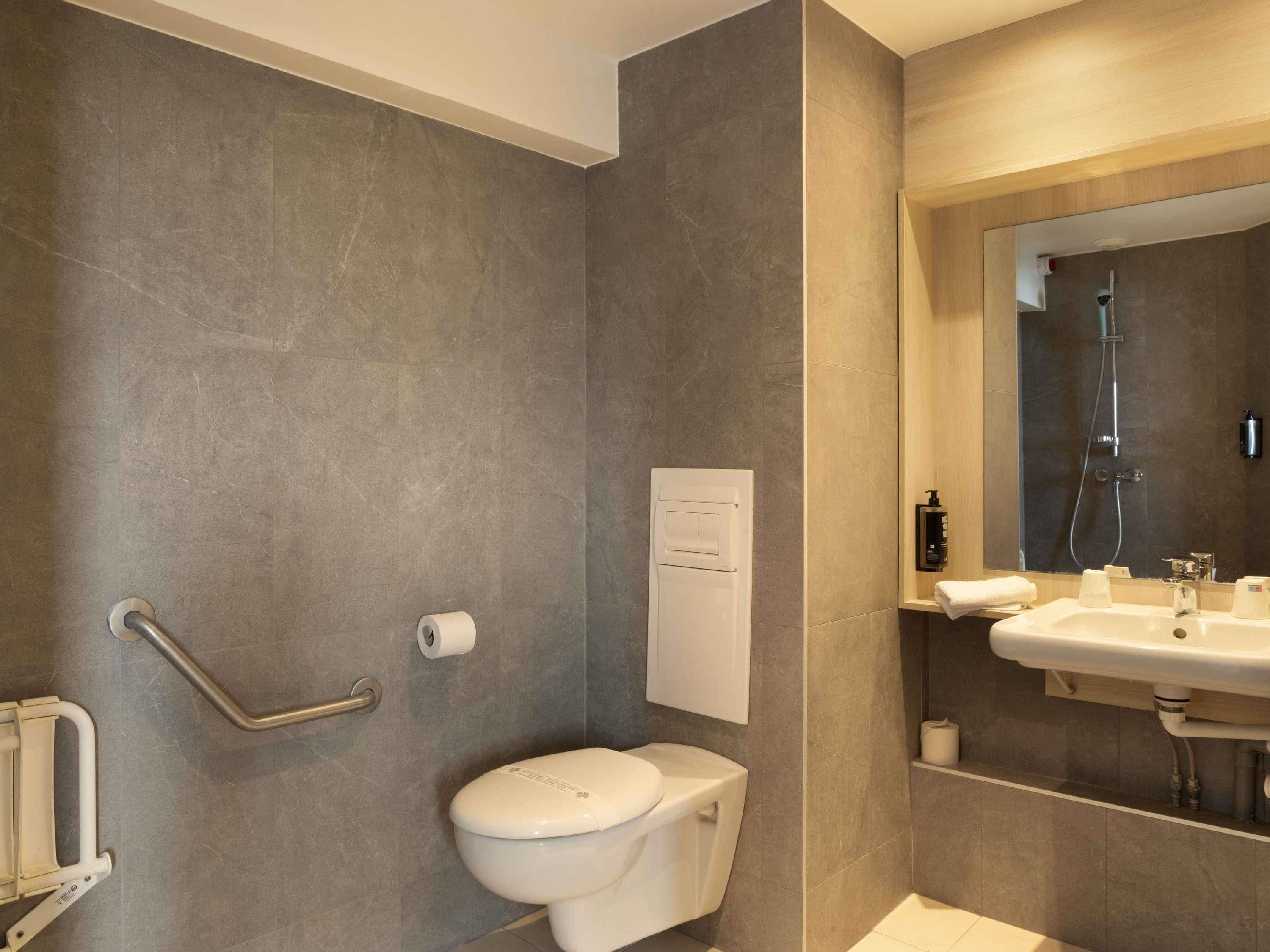 A modern bathroom with a toilet, a shower, a sink, and a handrail.