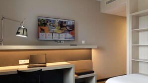 A hotel room with a desk, a laptop, a TV mounted on the wall, and two beds. - ibis Douai Dechy (Dechy)