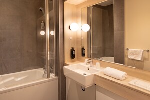 Un baño moderno con una bañera, un lavamanos y un espejo grande.