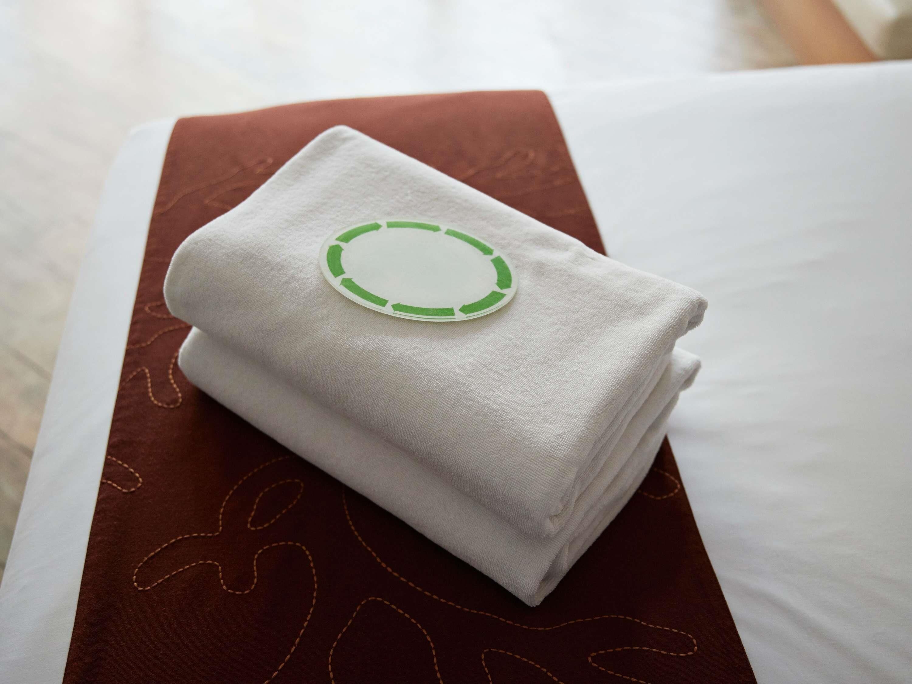 Une serviette blanche, soigneusement pliée, ornée d’un logo circulaire vert, posée sur un coussin marron.