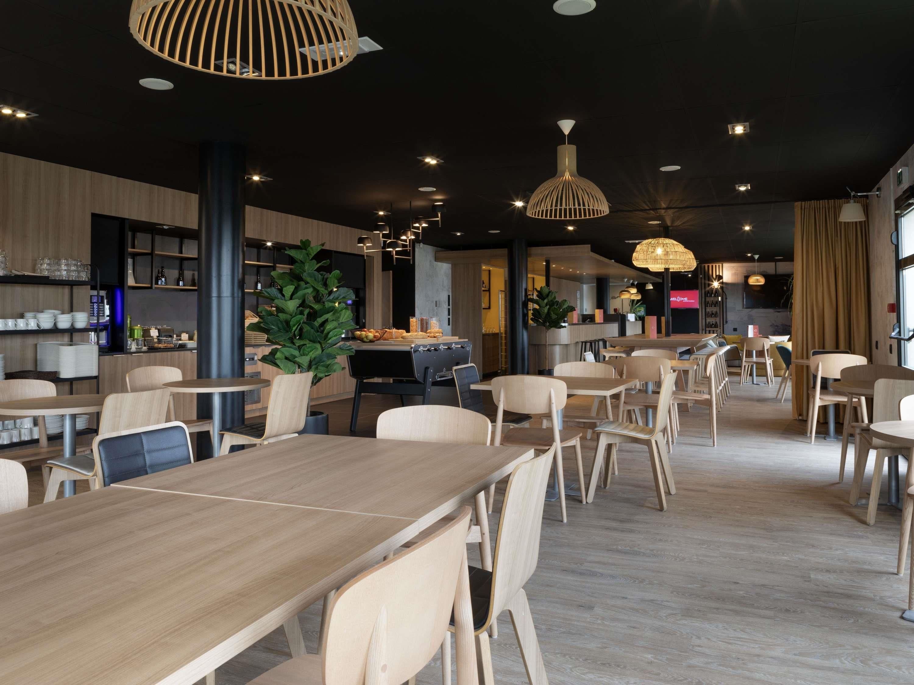 Een modern restaurantinterieur met houten tafels en stoelen, hanglampen en een bar.