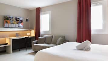Habitació d'hotel amb un llit, una taula de treball, una cadira, un televisor i cortines vermelles.