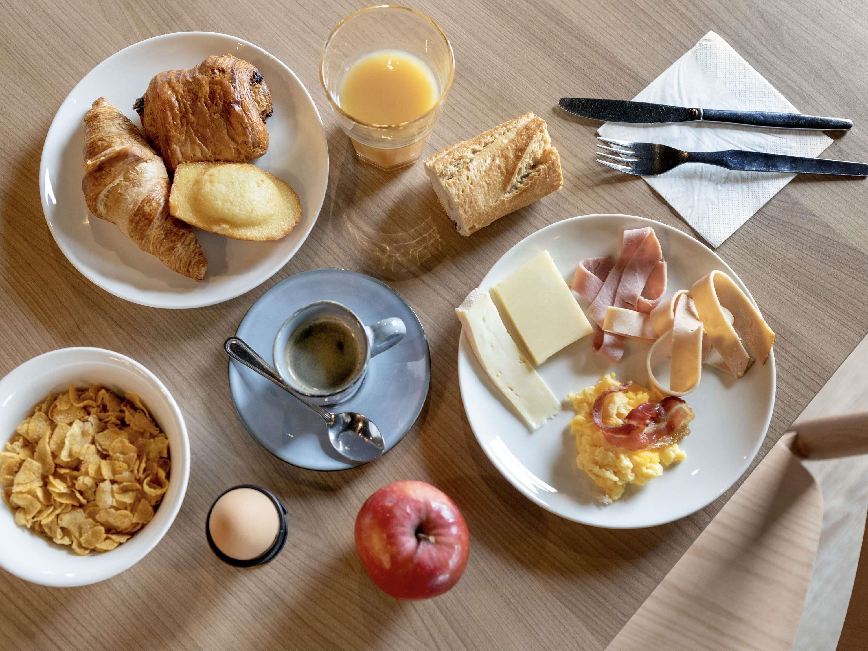 Aamiaispöytä, jossa on tarjolla croissantteja, appelsiinimehua, munakokkelia, kinkkua, juustoa ja muroja.