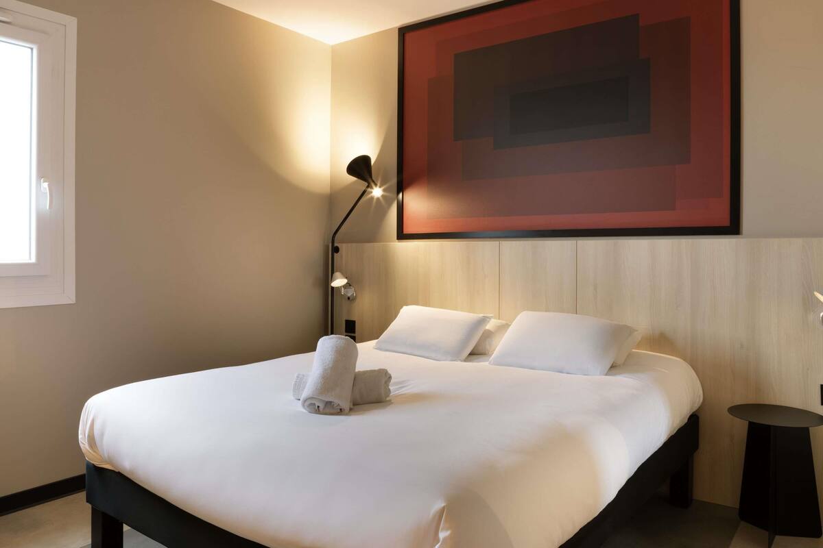 Habitación de hotel con una cama grande, una obra de arte colgada en la pared, una lámpara de noche y una mesita pequeña.