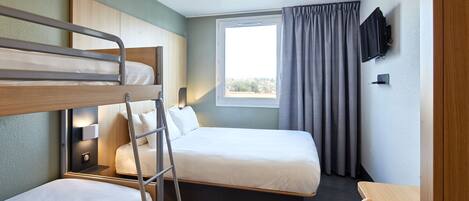 A hotel room with a bunk bed, a single bed, a desk, a chair, a TV, and a window with curtains.