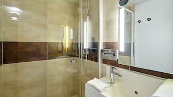 Un baño moderno con ducha acristalada, lavamanos blanco y un espejo grande.