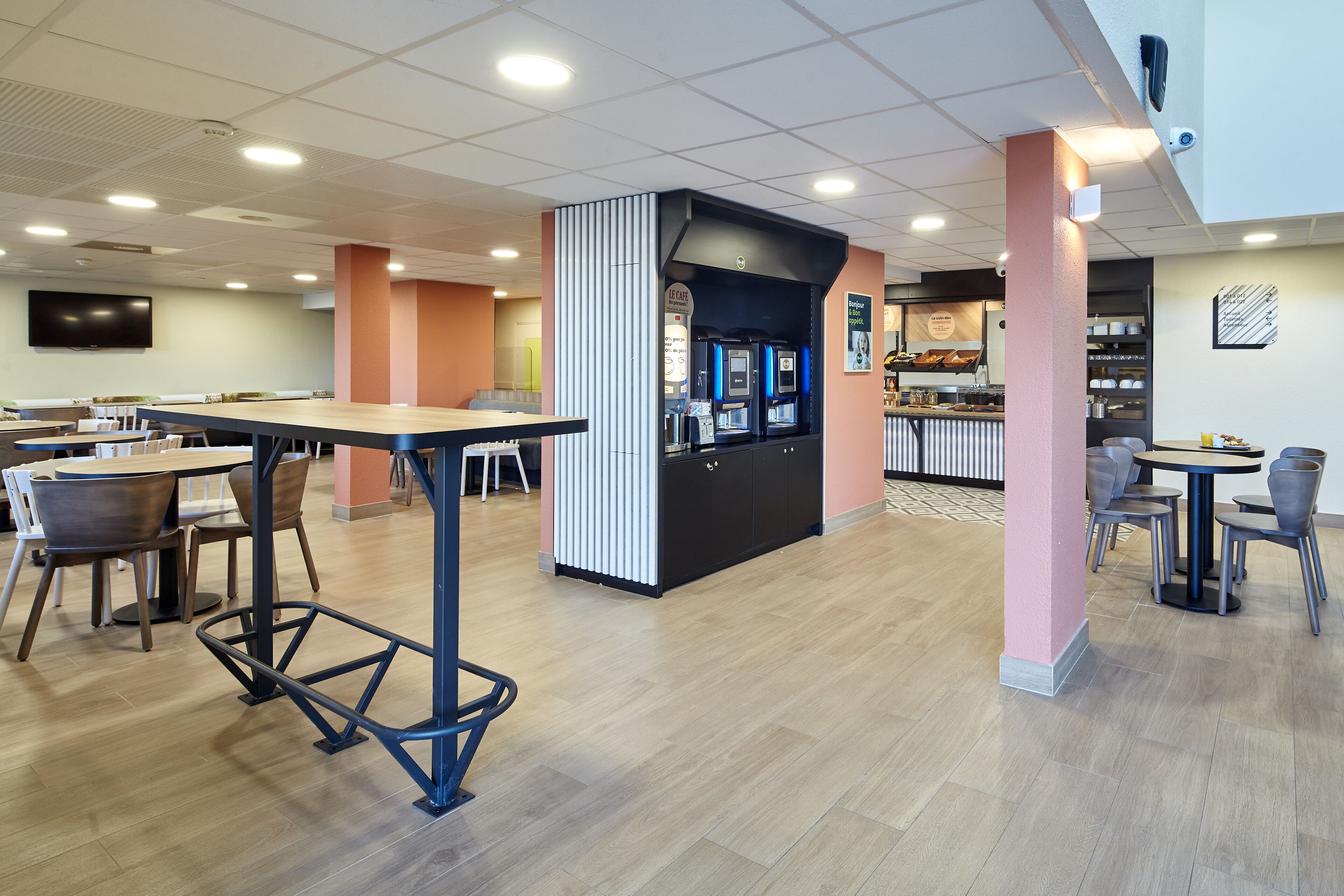 Un café moderno con mesas y sillas de madera, una barra de café y un televisor de pantalla plana en la pared.