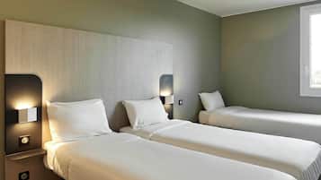 Habitación de hotel con dos camas individuales, una mesita de noche con lámpara y una ventana que deja entrar luz natural.