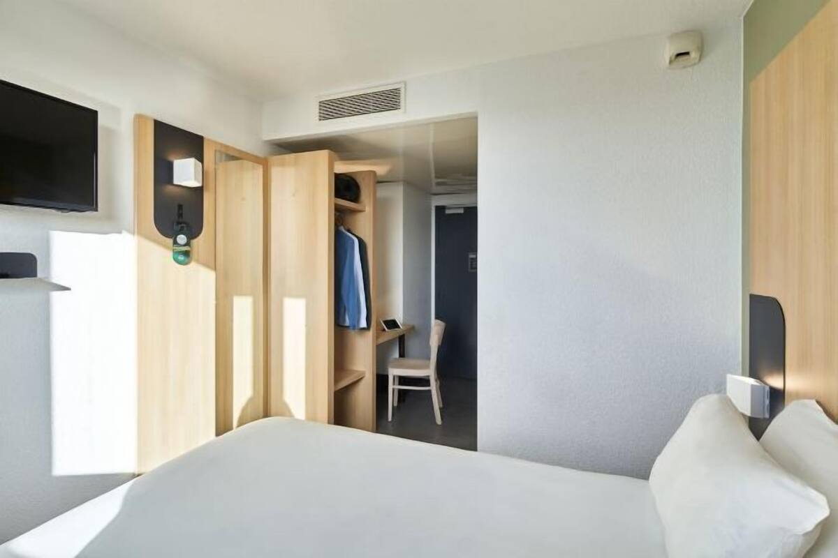 Une chambre d’hôtel comprenant un lit, une télévision, un bureau avec une chaise et une armoire.