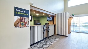 A reception area with a 'Bonjour & Bienvenue' sign, a reception desk, a television, and a patterned floor. - B&B HOTEL Paris Nord Gonesse Parc des Expos (Gonesse)