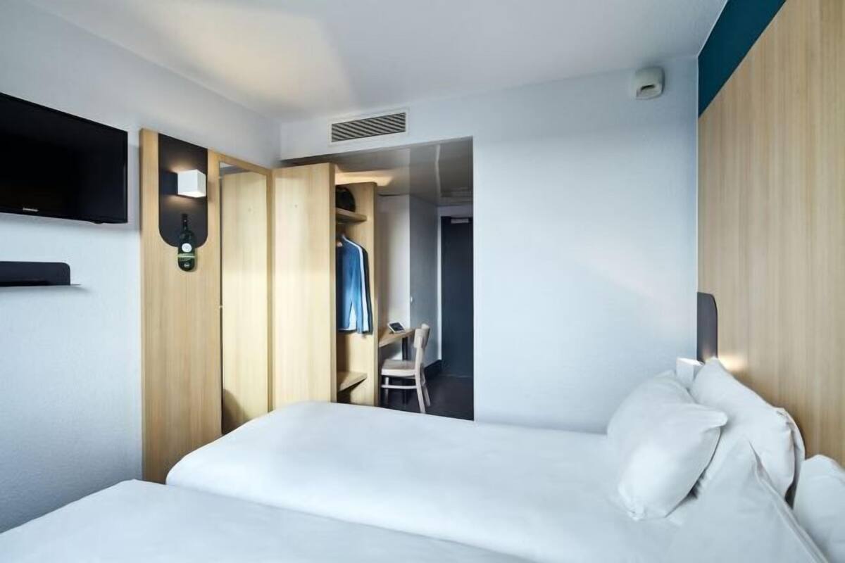 Une chambre d’hôtel comprenant un lit, un téléviseur fixé au mur, une armoire avec un miroir et un bureau avec une chaise.