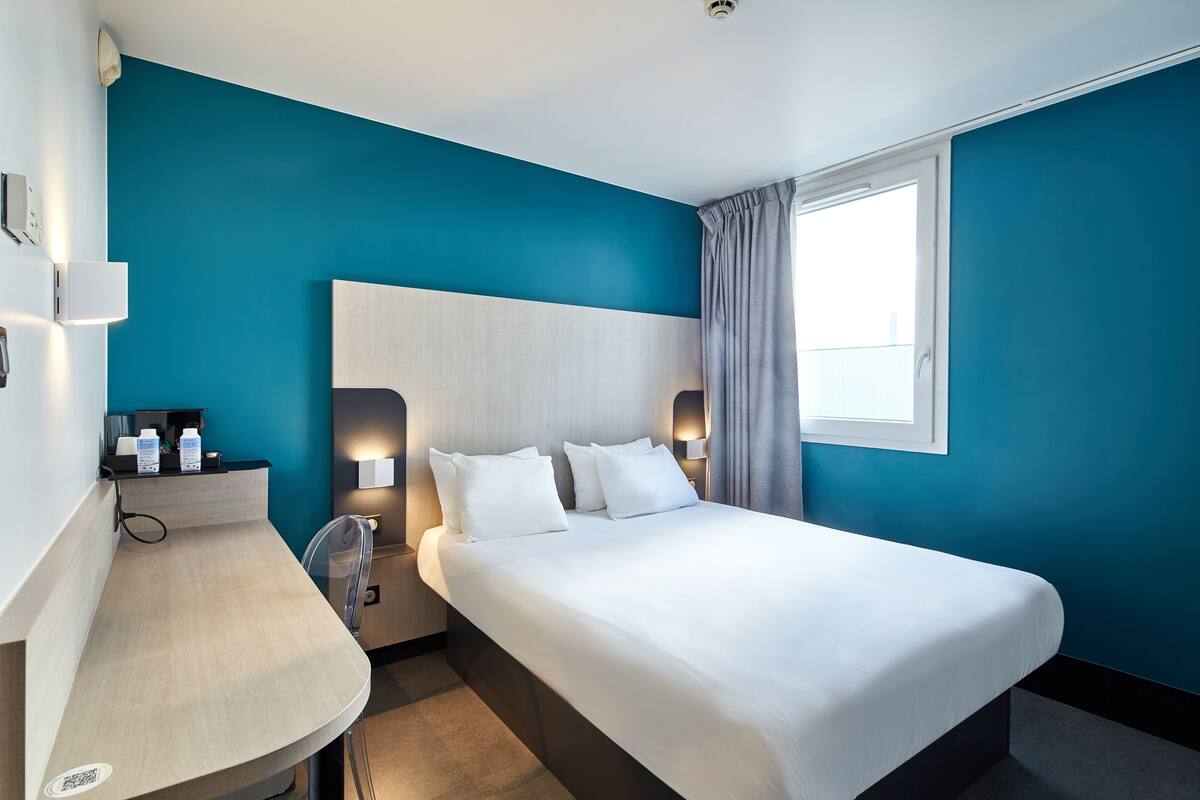 Une chambre d’hôtel moderne avec un grand lit, une table de chevet, une commode et une fenêtre avec des rideaux.