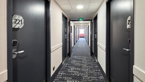 A hotel hallway with doors numbered 221 and 222, featuring a black carpet with white text and a green exit sign. - B&B HOTEL Paris Nord Gonesse Parc des Expos (Gonesse)