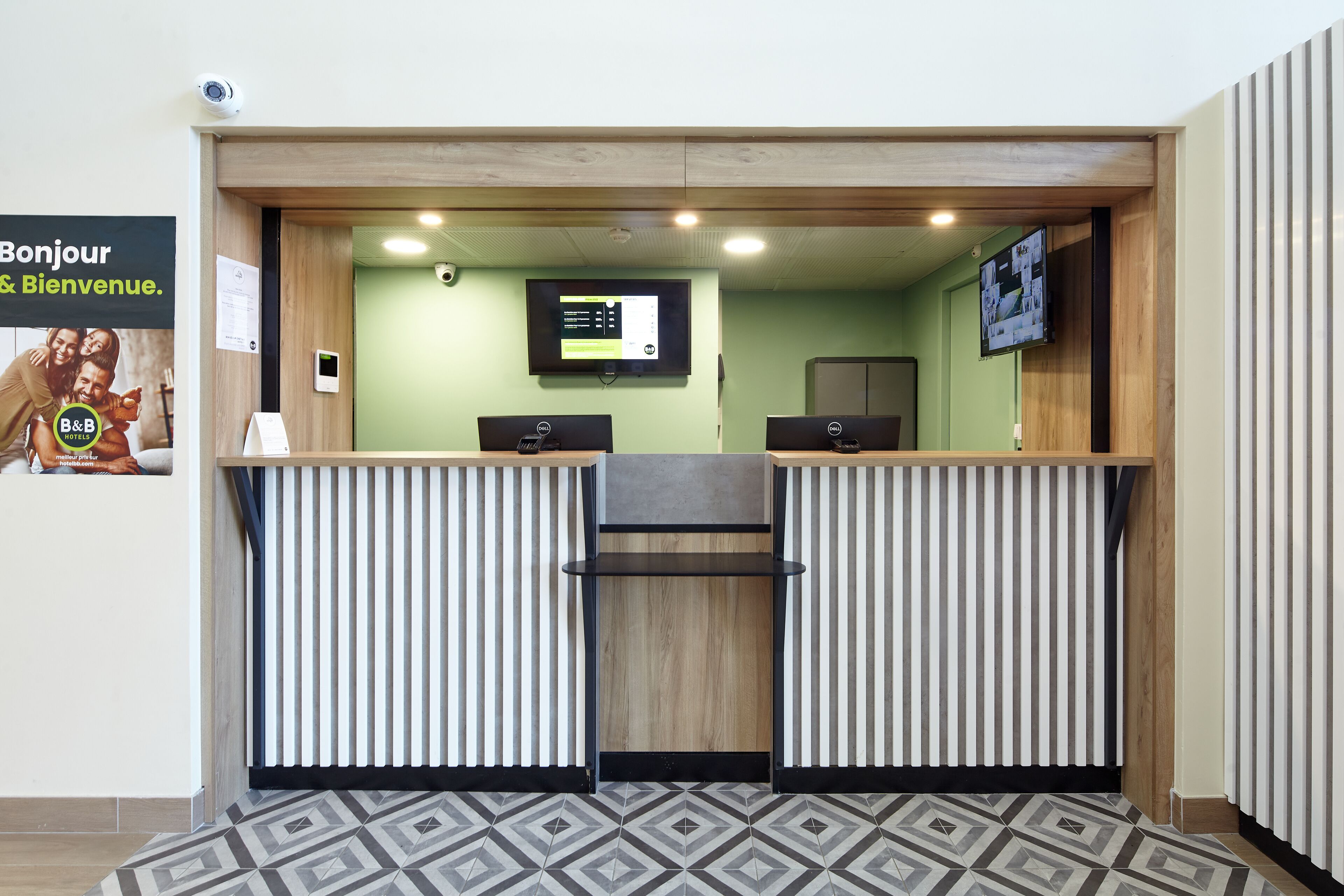 A reception desk with a digital screen, two computer monitors, and a wooden counter.