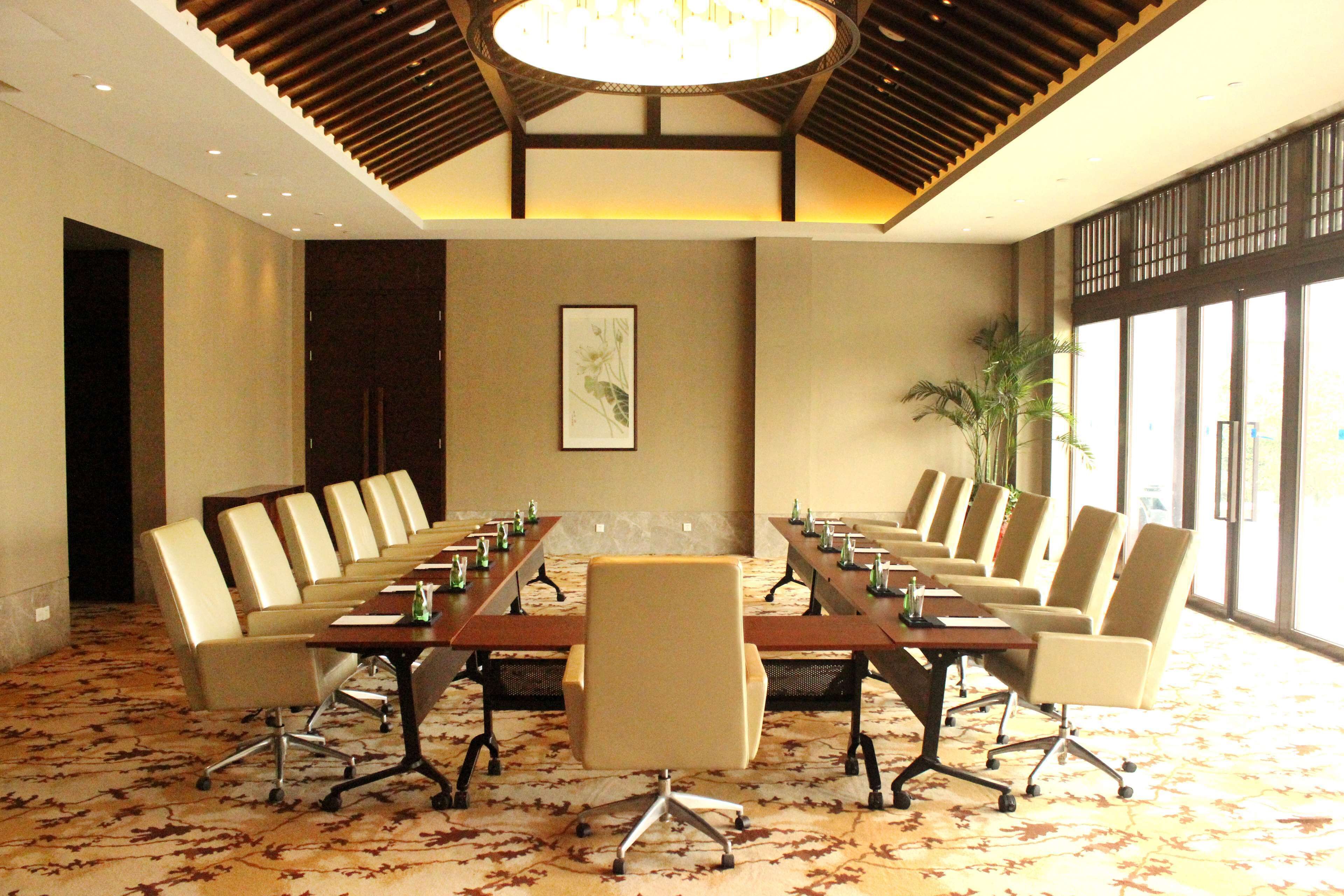 Sala de conferências com uma mesa comprida e várias cadeiras, janelas amplas e teto com design em madeira.