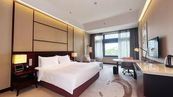 Quarto de hotel com uma cama grande, uma escrivaninha, uma cadeira, uma televisão e uma janela com cortinas.
