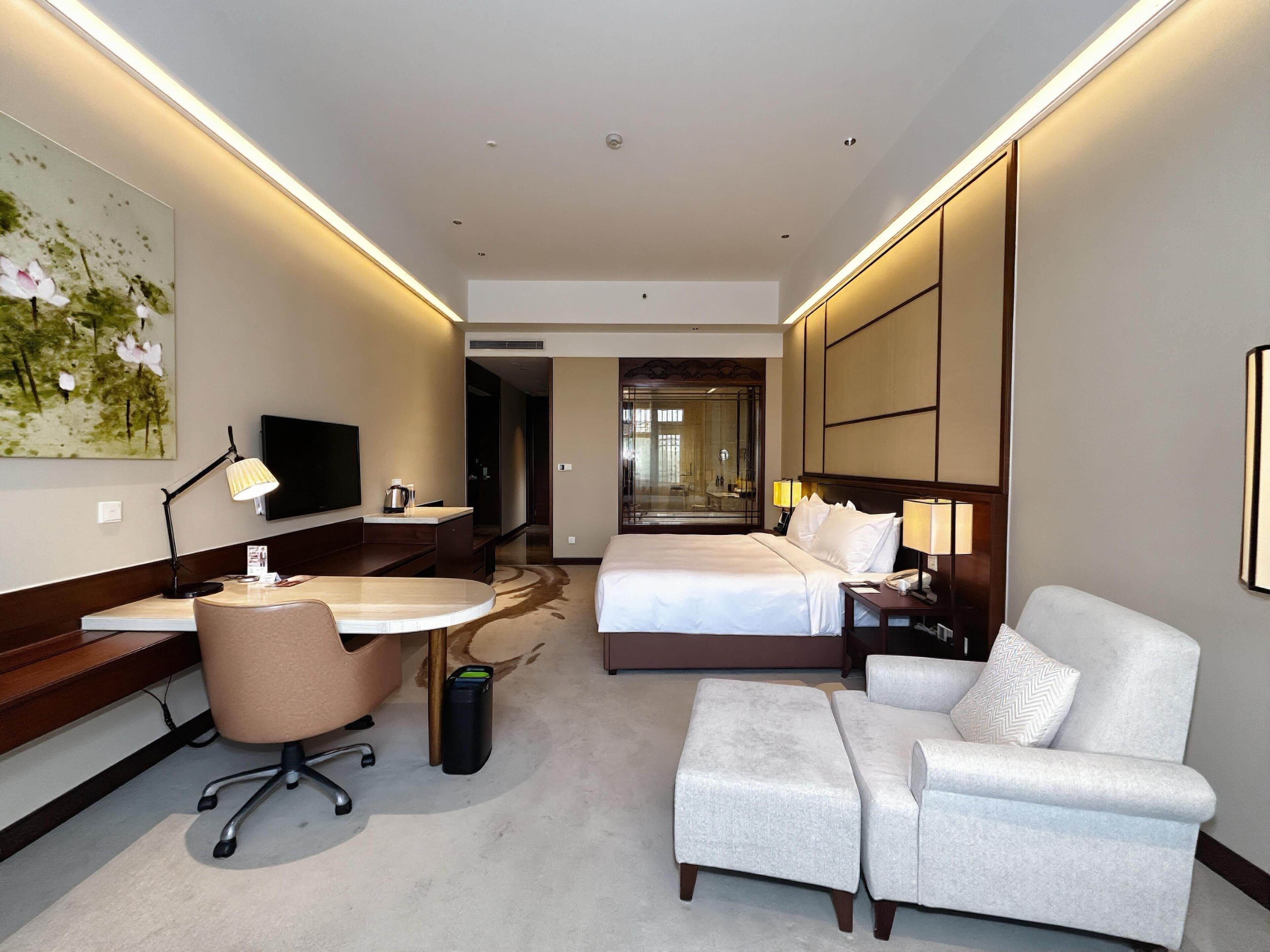 Una habitación de hotel con una cama, un escritorio con silla, un sofá, un televisor y un cuadro en la pared.