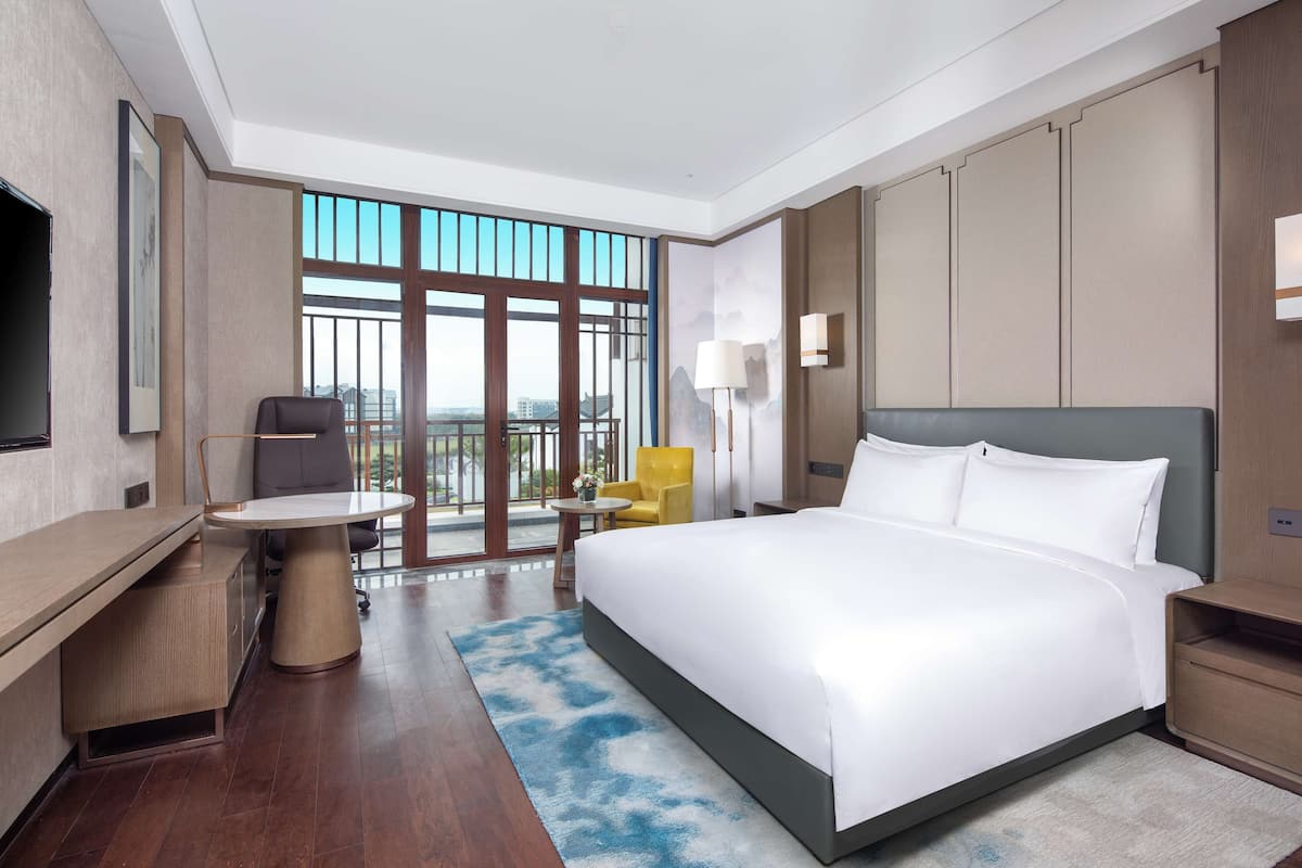Habitación de hotel con una cama grande, un escritorio, una silla, una mesita y un balcón con vistas.