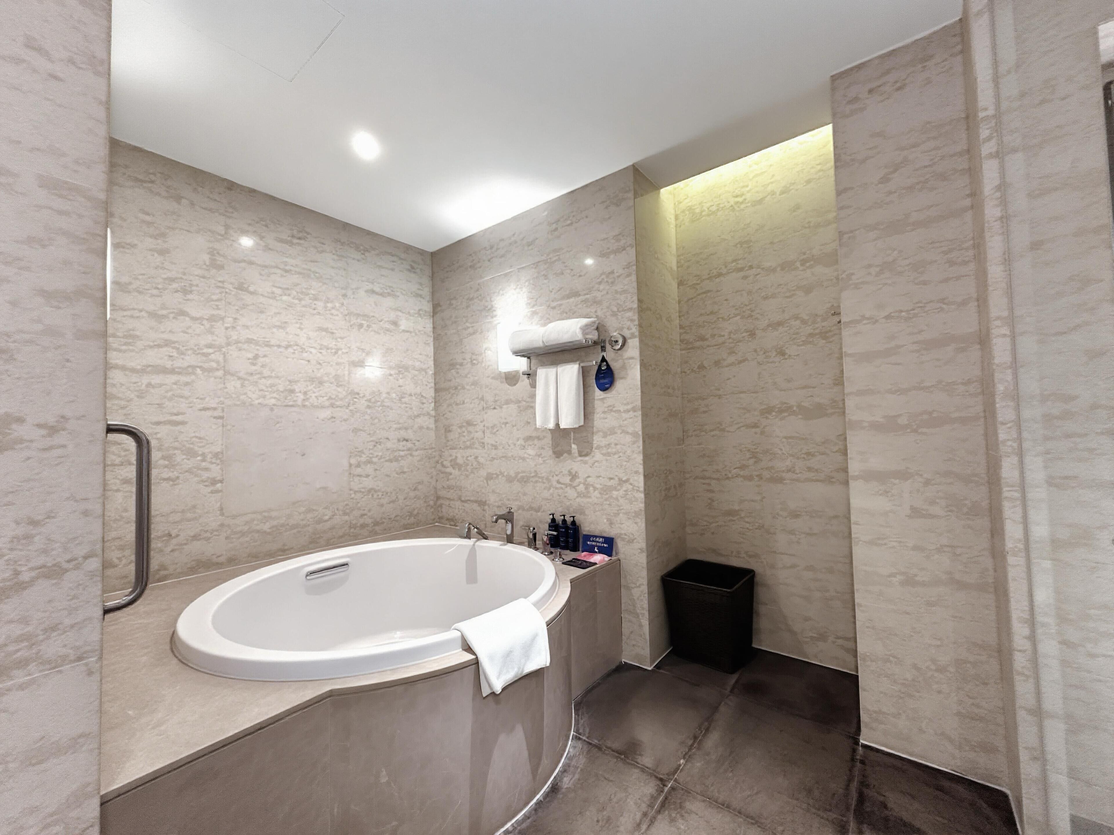 A modern bathroom with a freestanding bathtub, a towel rack, and a trash bin.