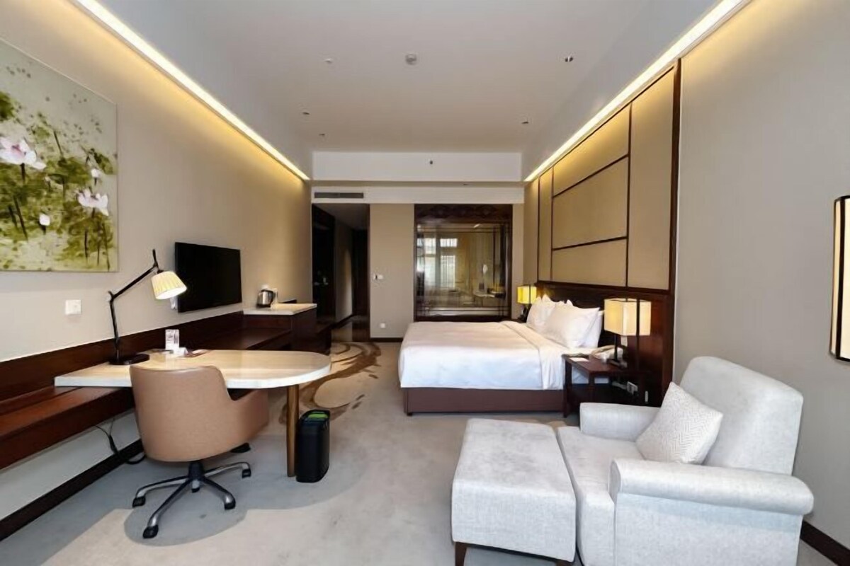 Hotelkamer met een bed, bureau, stoel, bank, televisie en schilderij aan de muur.