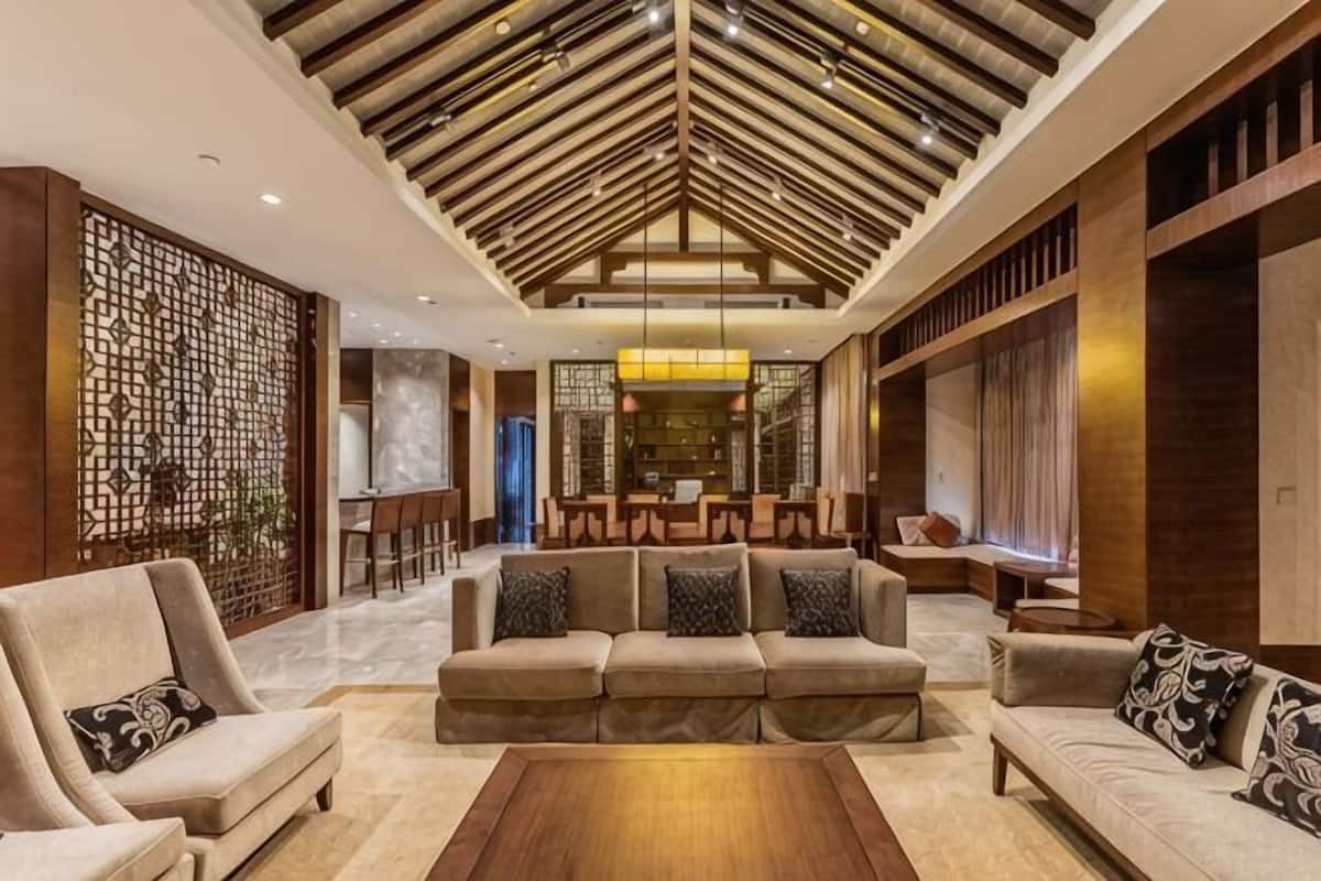 A spacious living area with a high ceiling, a sofa set, a coffee table, and a dining area in the background.