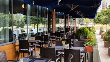 An outdoor restaurant with tables and chairs, large umbrellas, and a view of the street.