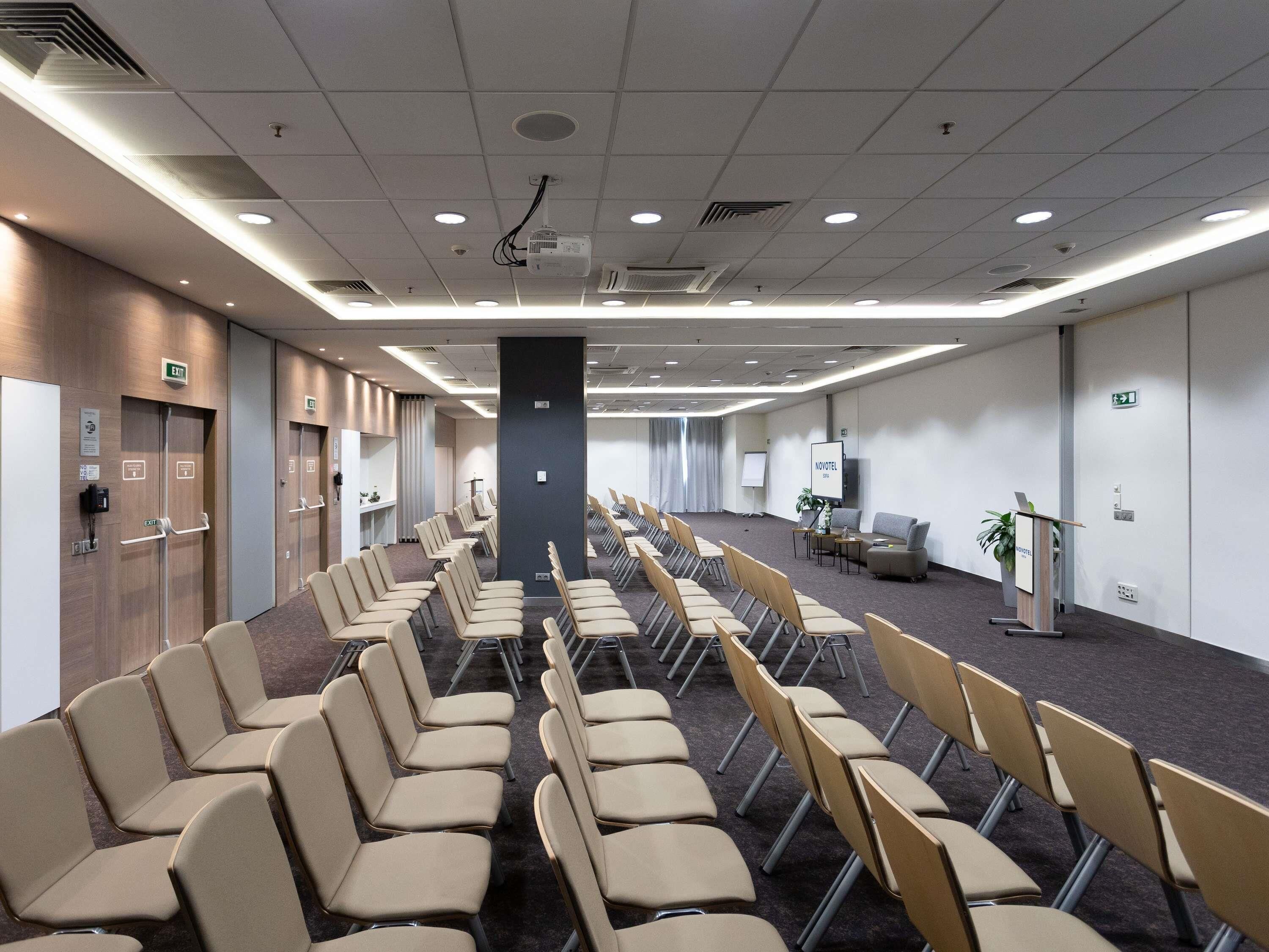 A conference room with rows of chairs, a podium, and a projection screen.