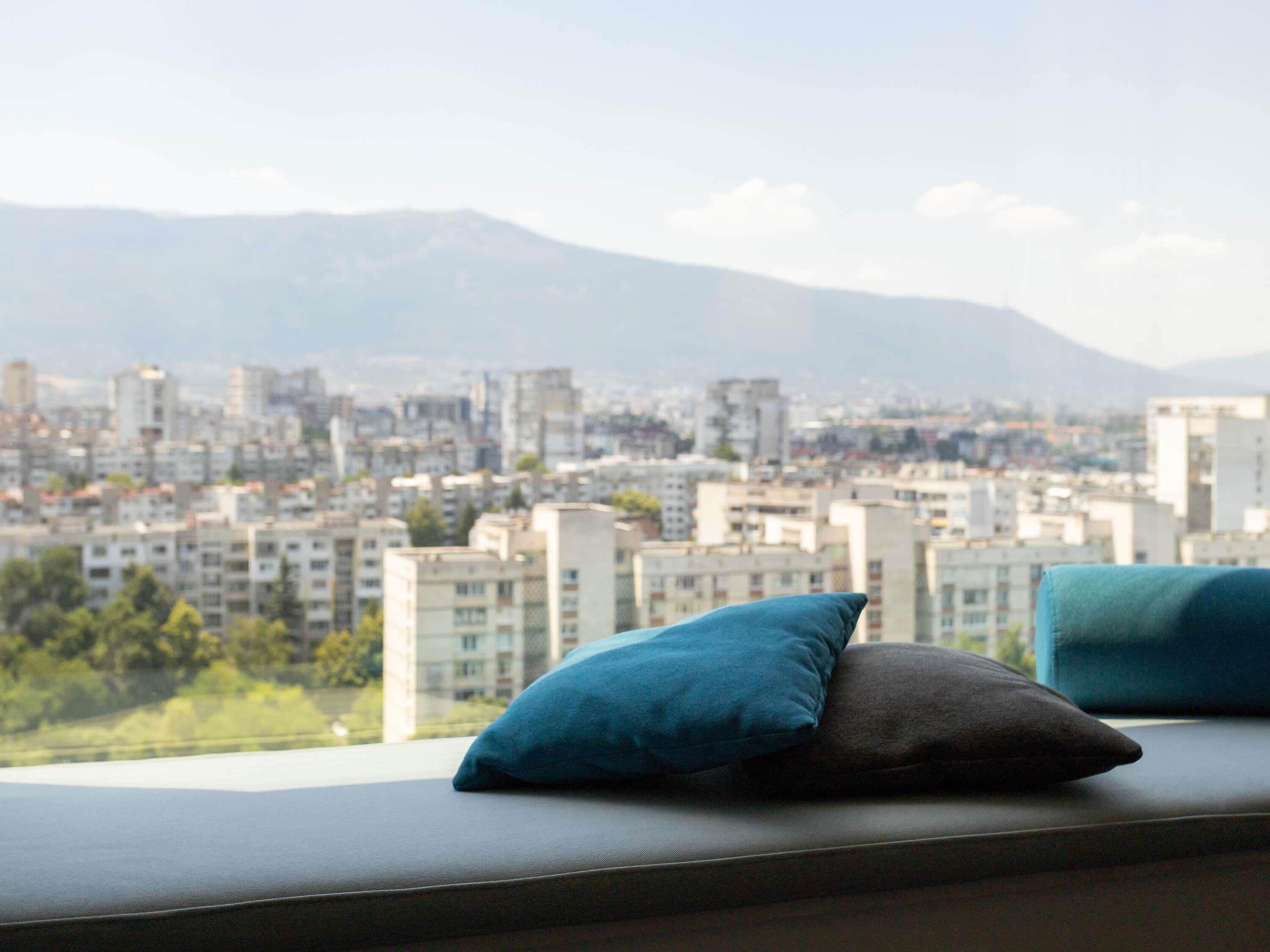 Vista panorámica de la ciudad desde una ventana con un sofá y cojines.