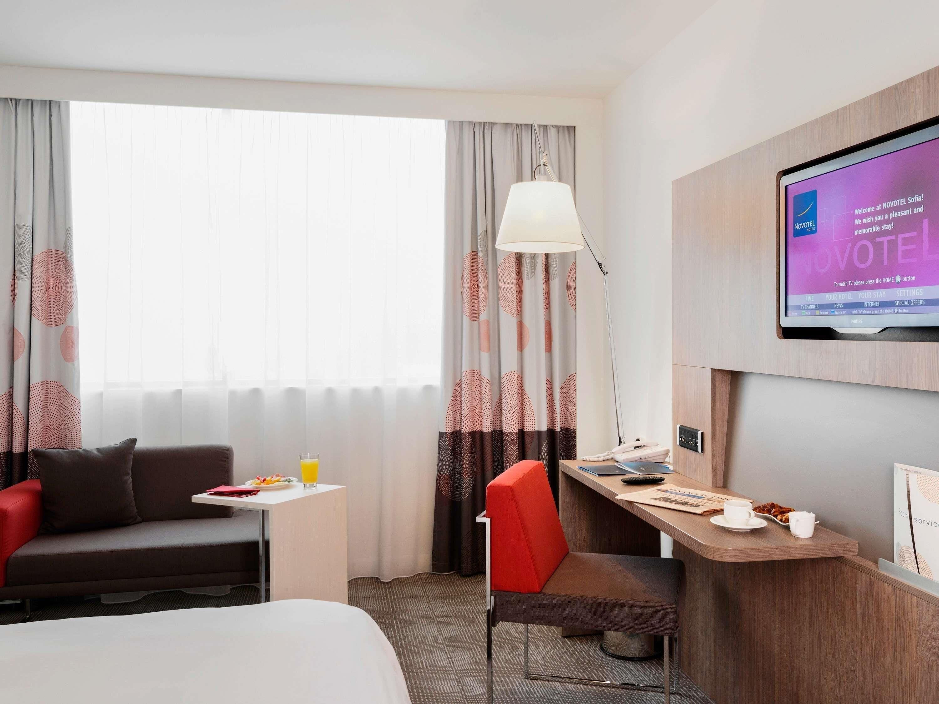 A hotel room with a bed, a desk, a chair, a TV, and a window with curtains.