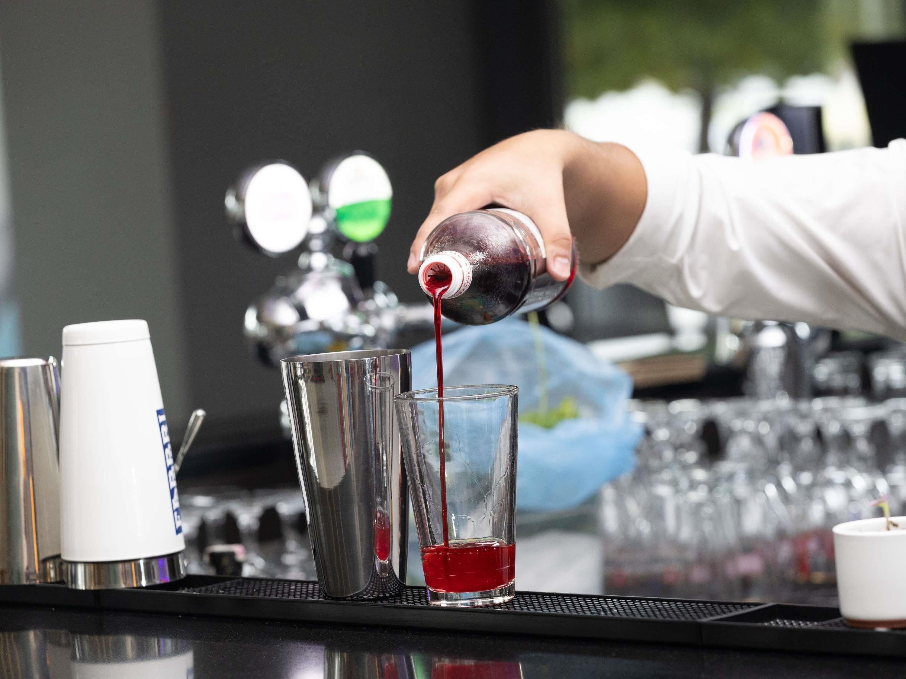 A bartender pouring a red liquid into a glass.