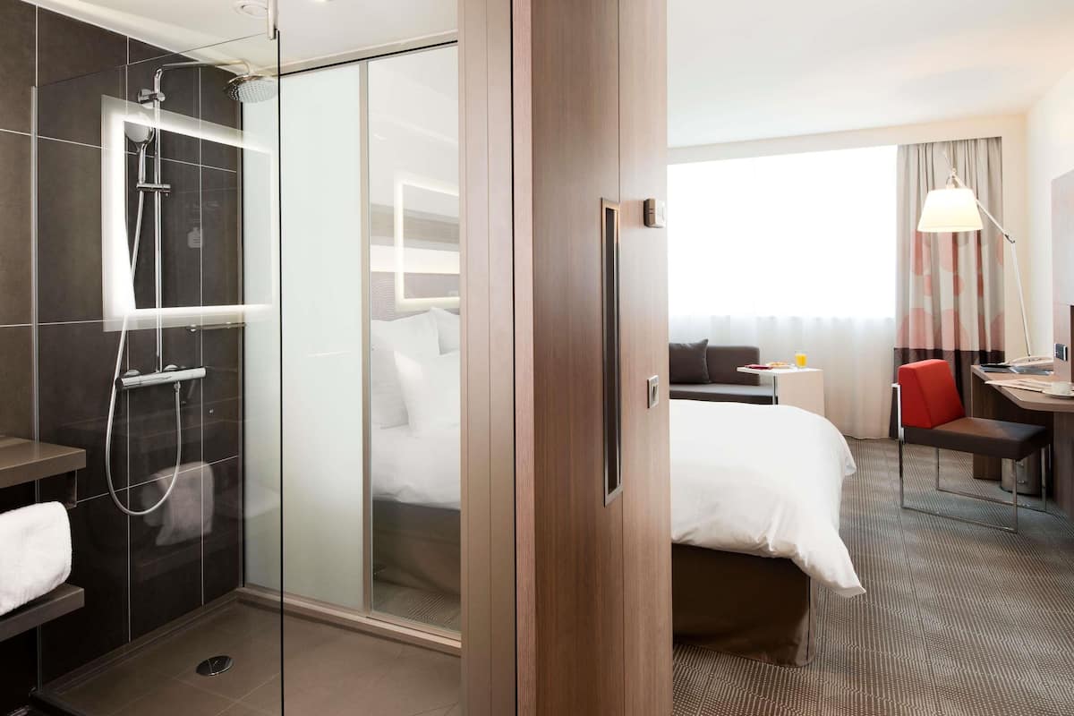 Habitación de hotel con ducha, cama, escritorio y vistas al exterior.