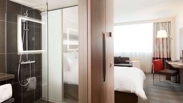 Habitación de hotel con ducha, cama, escritorio y vistas al exterior.